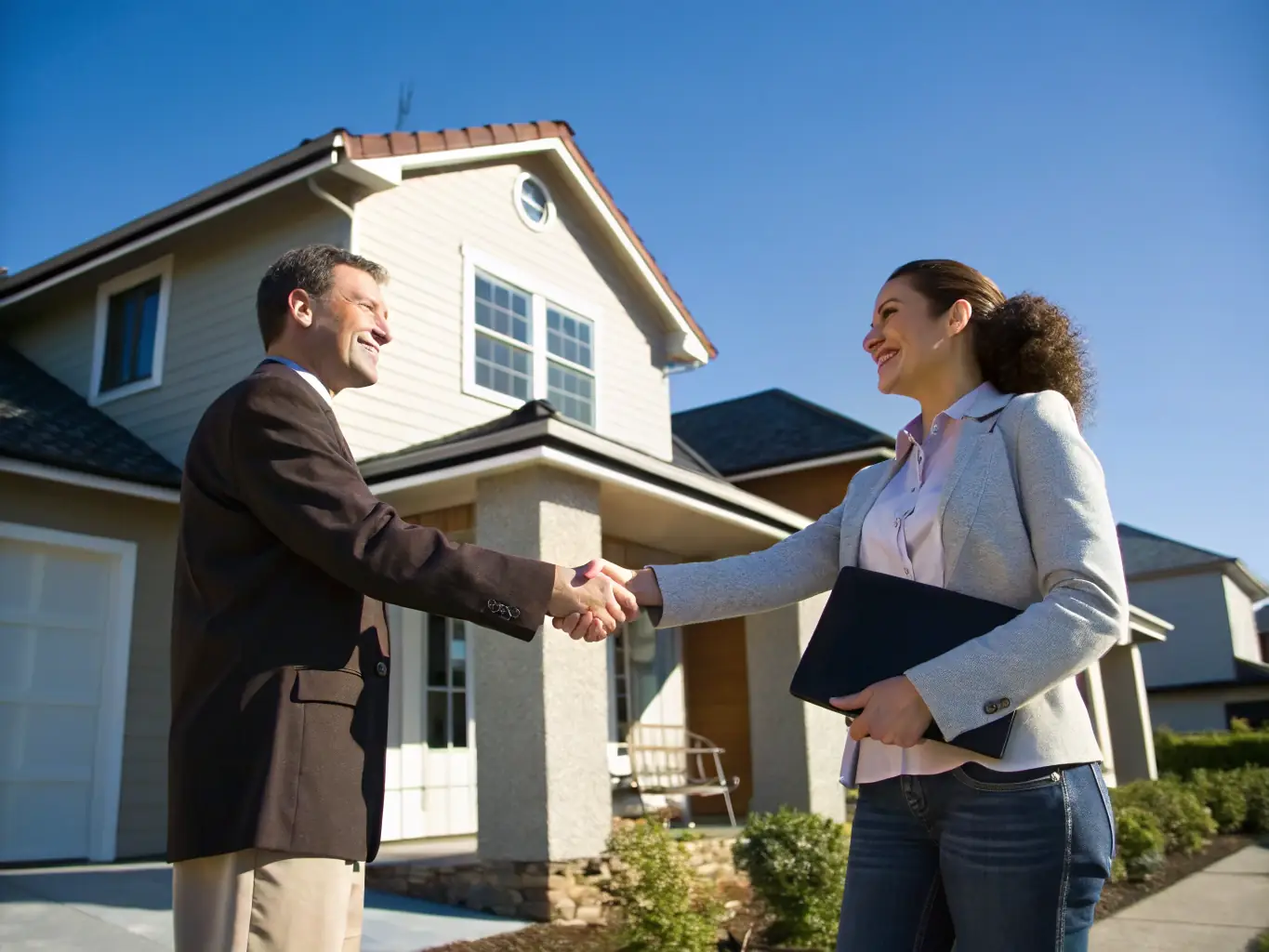 A real estate agent shaking hands with a satisfied client in front of a luxury property, representing a successful transaction.